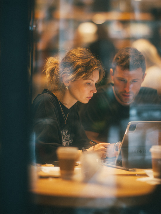 Two professional marketeers brainstorm on iPads over a coffee.